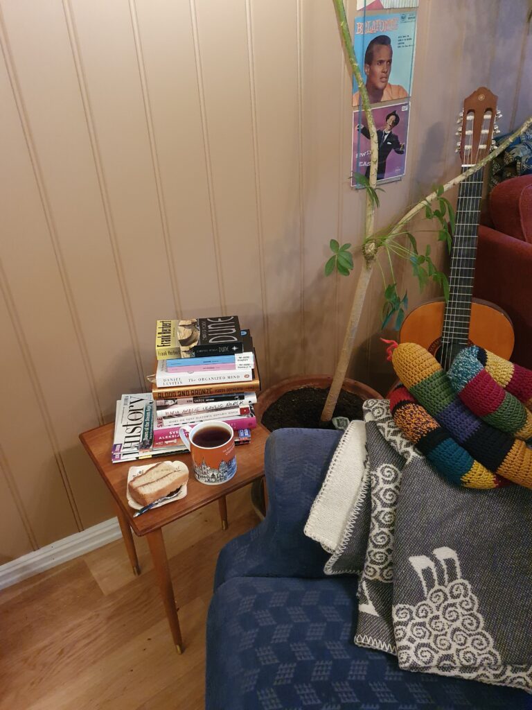 Fotografi av en lenestol, en stabel med bøker, en kopp te og et kakestykke.