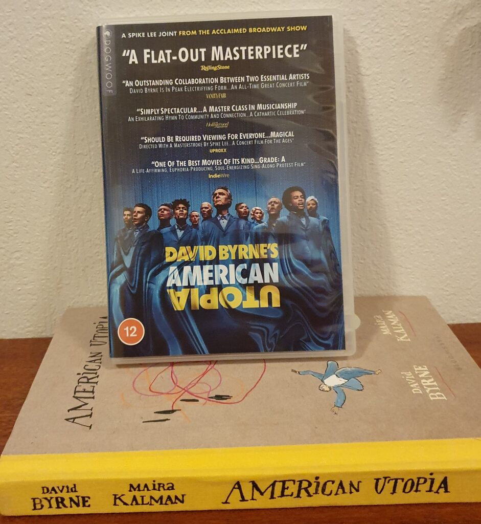 DVD-en American Utopia og boka American Utopia. På ryggen til boka står navnene David Byrne og Maira Kalman. Øverst på DVD-en står det "A flat-out masterpiece".