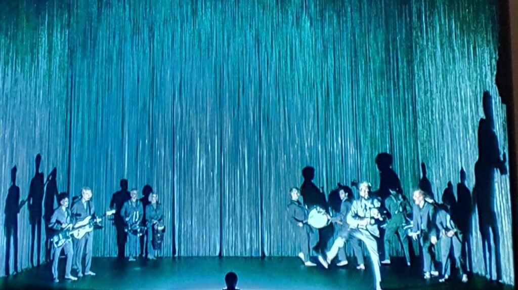 Stillbilde fra filmen. Mennesker danser på en gråblå scene.